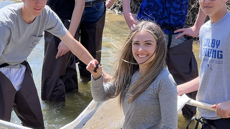 A smiling young woman holds a crayfish caught during a stream study.