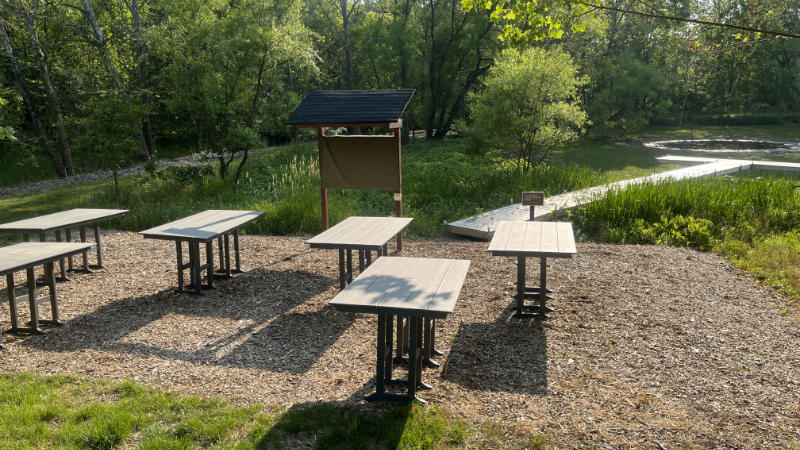 An outdoor learning space with tall tables and signboard.
