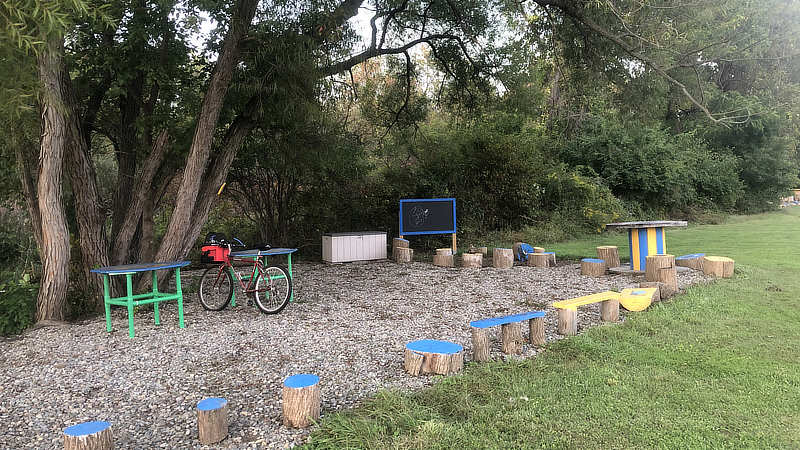 An outdoor classroom with tree stump seats and benches and a chalkboard.