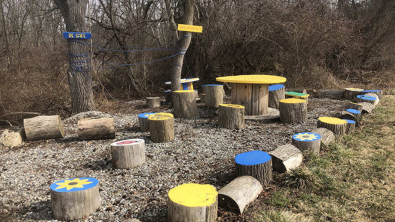 Tree stump seating painted with flowers and insects in an outdoor classroom.